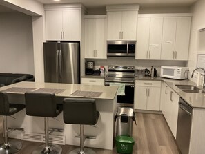 A modern kitchen with stainless steel appliances, a central island with bar stools, and a green trash bin. - 3 BEDROOM DUPLEX, 7 minutes to Train statio, 3 minutes to Anthony Henday, (Edmonton)
