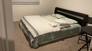 A bedroom with a bed, a chair, a window, and a wall.