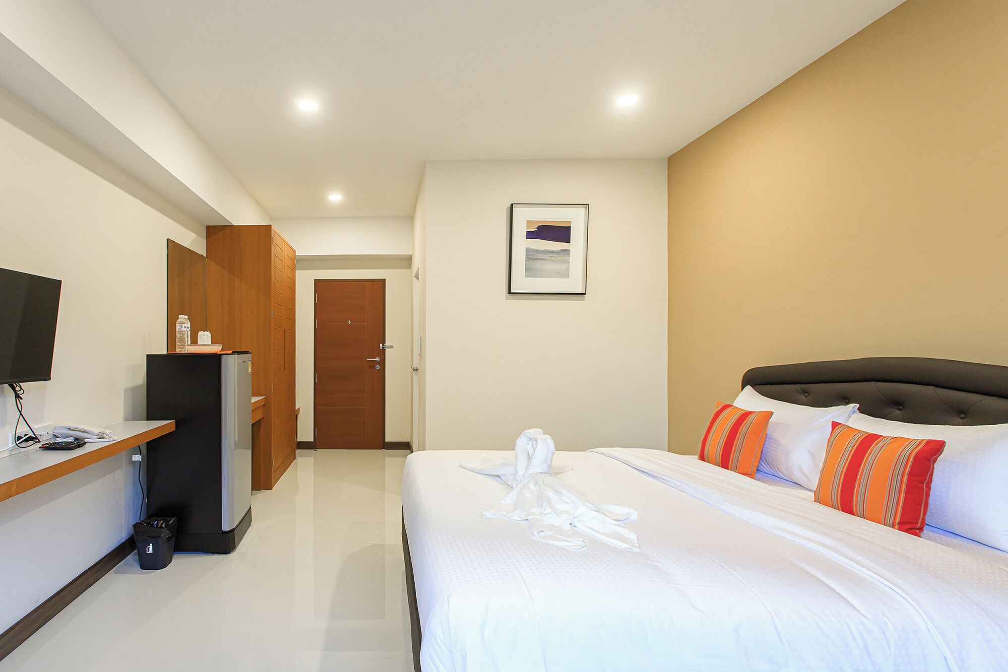 A hotel room with a bed, a desk with a computer, a TV, and a door.