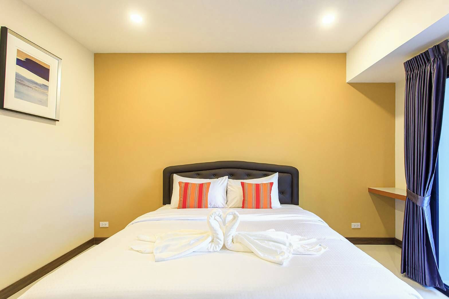 Une chambre d’hôtel avec un lit, un tableau encadré au mur et un rideau à la fenêtre.