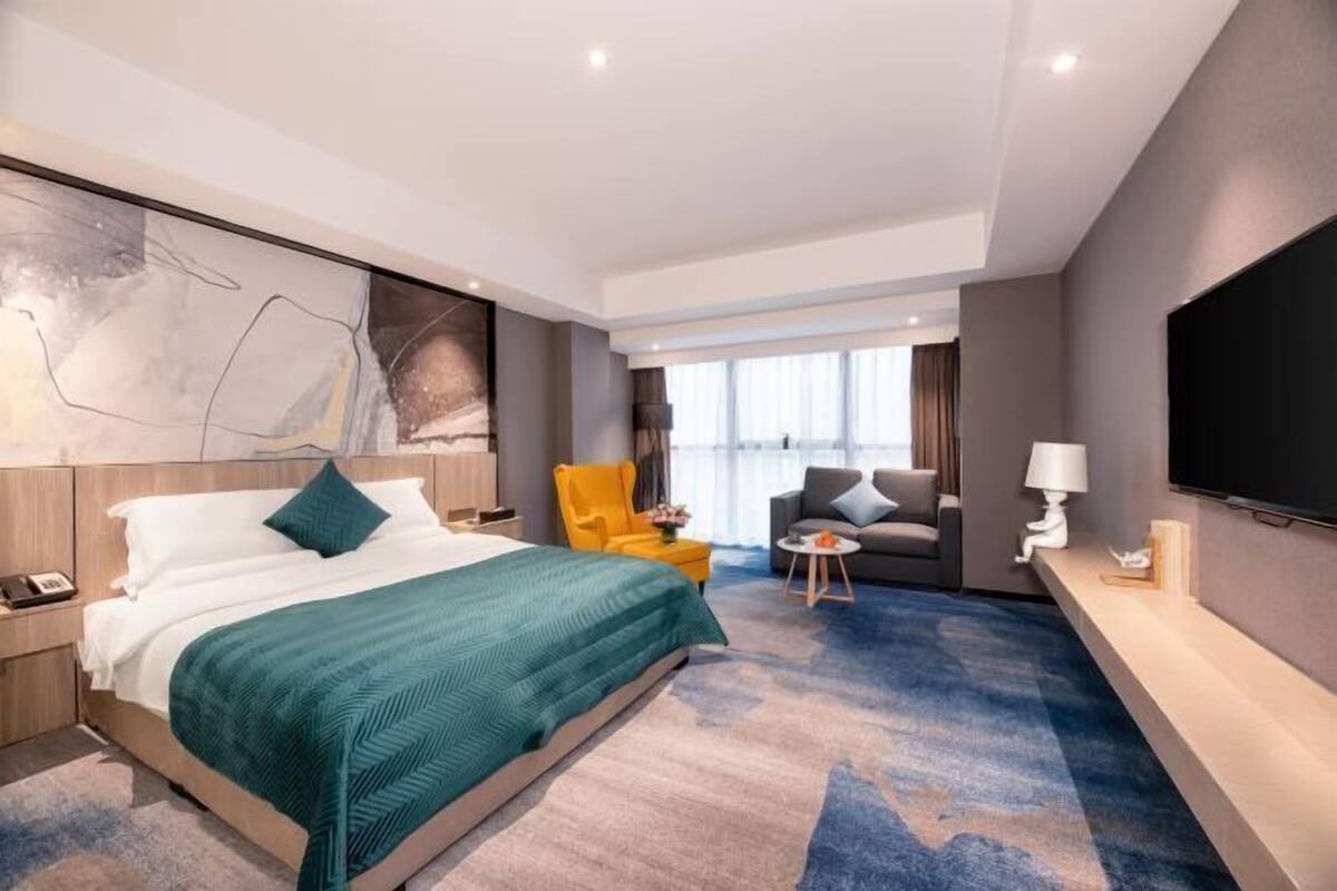 Une chambre d’hôtel avec un lit, un canapé, une chaise, une télévision et une fenêtre.