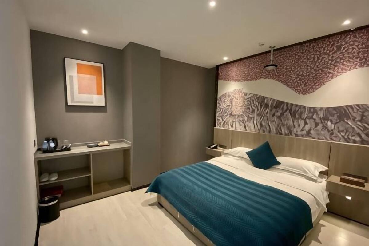 Une chambre d’hôtel moderne équipée d’un lit, de tables de chevet, d’un bureau et d’une œuvre d’art accrochée au mur.