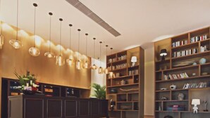 Eine geräumige Lobby mit einem hölzernen Empfangstresen, mehreren hängenden Pendelleuchten und einem großen Bücherregal voller Bücher und Dekoration.