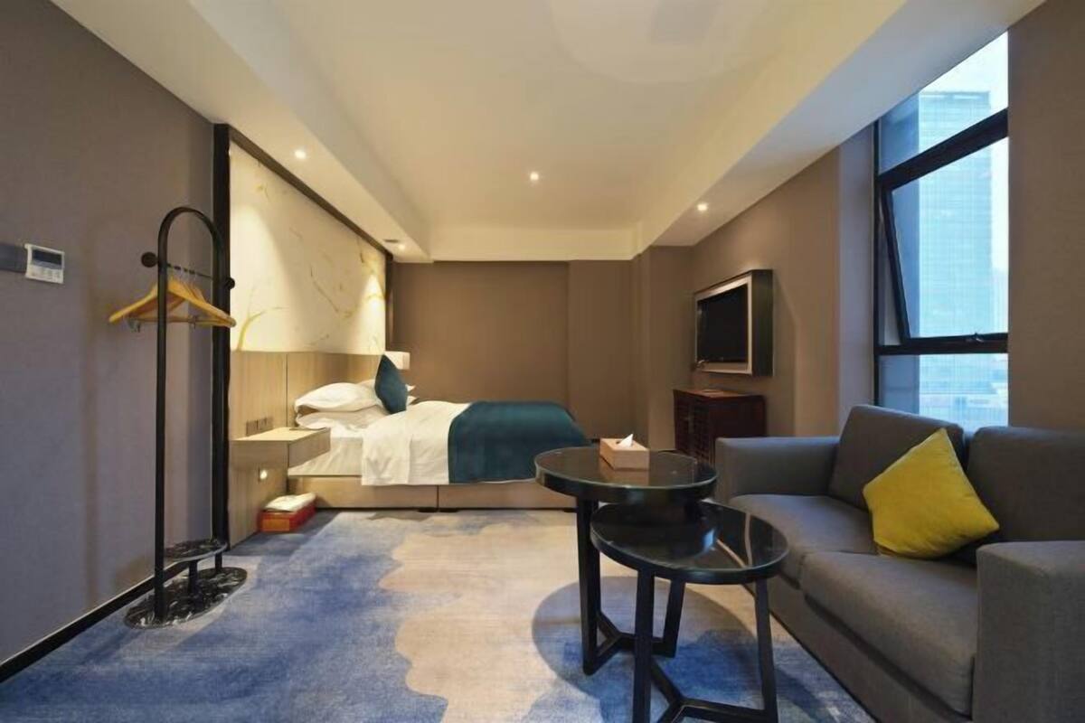 Une chambre d’hôtel avec un lit, un canapé, une petite table, une télévision et une fenêtre donnant sur la ville.