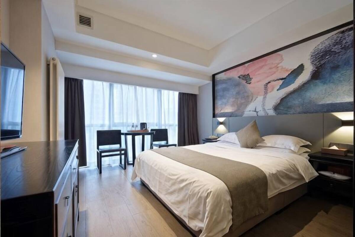 Une chambre d’hôtel avec un lit, un bureau, une télévision et un grand tableau au mur.