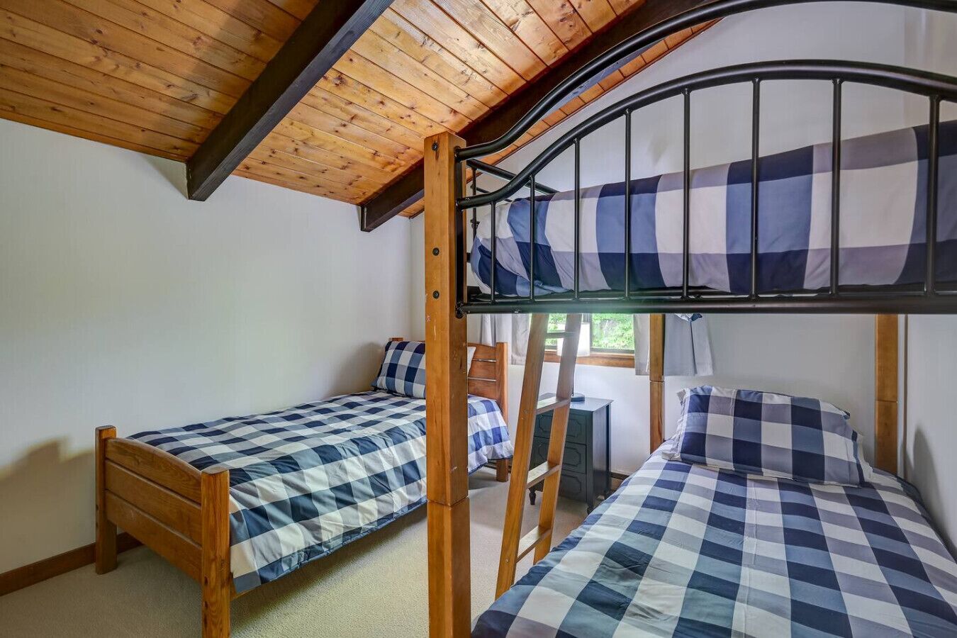 A dormitory room with two wooden bunk beds, each with a checkered blue and white bedding.