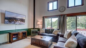 A living room with a large TV, a fireplace, a sofa, and a view of the outdoors.