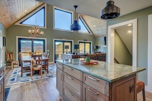 A spacious kitchen with a large island, wooden cabinets, and a view of the mountains through the windows. - LUX: Best View in Jackson | Hot Tub | New Home (Jackson)