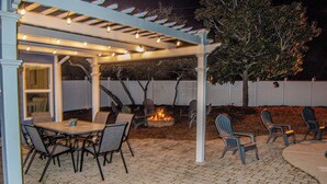 An outdoor patio with a covered seating area, a fire pit, and a pergola with string lights. - Marvelous 4-bedroom house with AC in Miramar Beach (Miramar Beach)