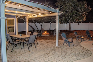 Une terrasse extérieure dotée d’un espace salon couvert, d’un foyer et d’une pergola illuminée de guirlandes lumineuses.