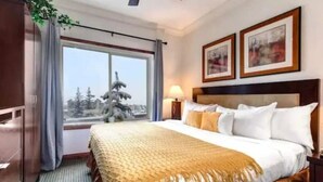 A hotel room with a large bed, a window with a view of trees, and two framed pictures on the wall.