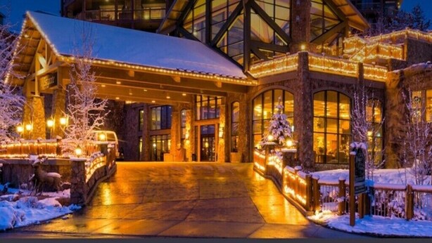A lodge with a large entrance, stone walls, and a covered porch with lights.