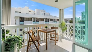 En balkon med et bord, stole, en potteplante og udsigt til bygninger.