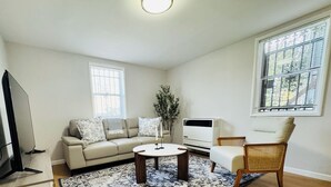 Een woonkamer met een bank, een salontafel, een televisie en een raam met zonwering.