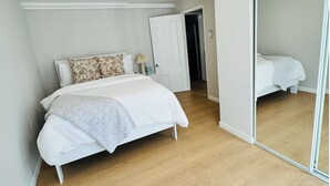 Een slaapkamer met een bed, een nachtkastje, een spiegel en een deur die naar een andere kamer leidt.