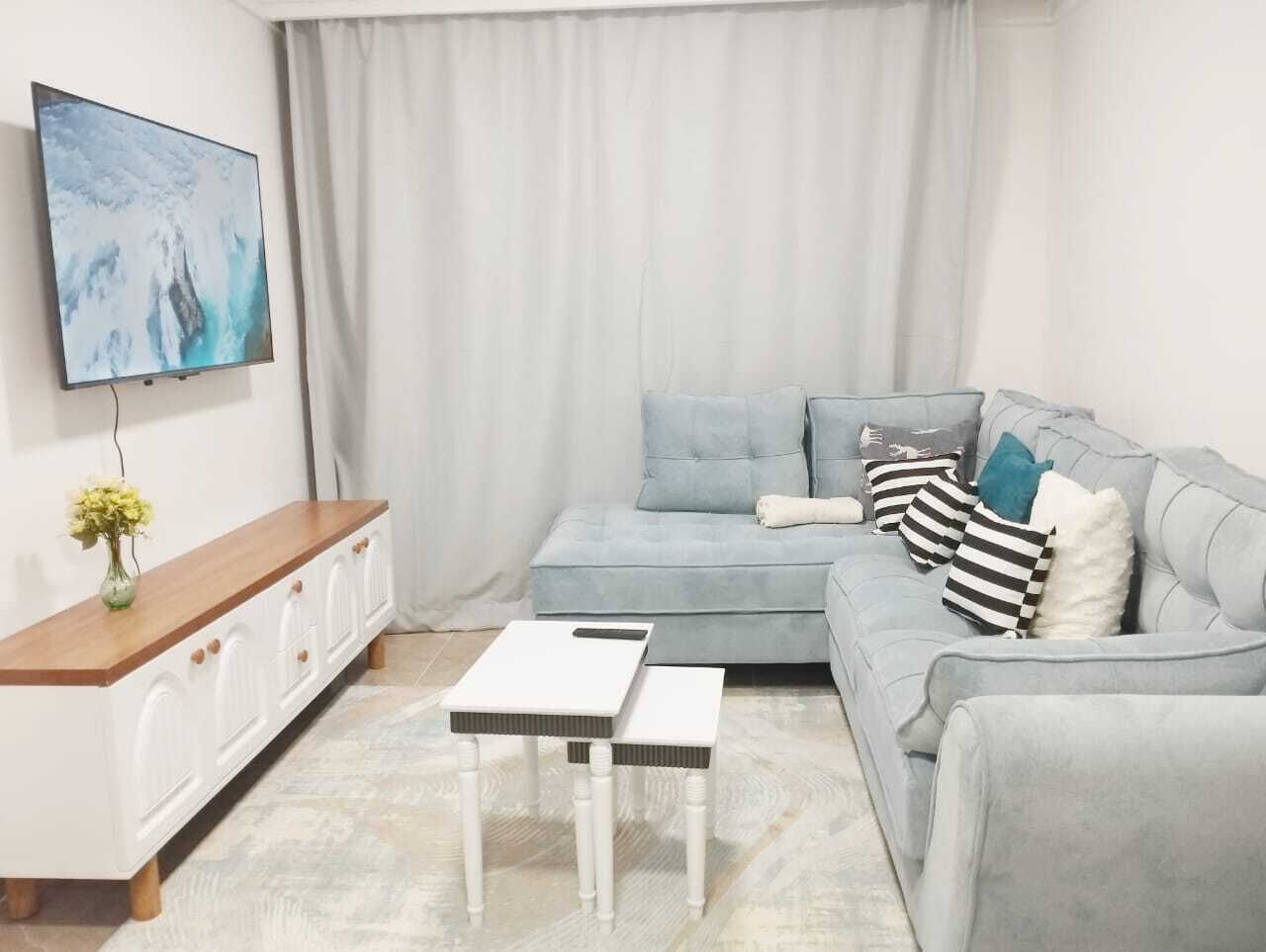 Un salon avec un canapé gris, une table basse blanche et un téléviseur fixé au mur.