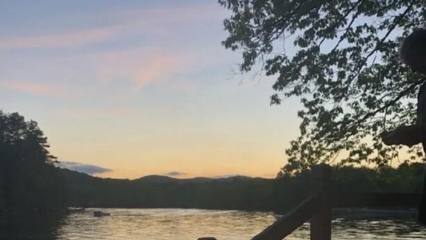 Un hogar de fuego en una terraza de madera con vista a un lago tranquilo al atardecer.