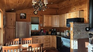 Interior acogedor de una cabaña con paredes de madera, una zona de comedor con sillas y una mesa, una cocina con electrodomésticos y una chimenea.