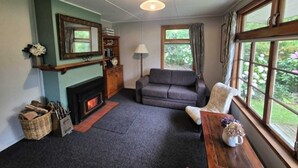 Una sala de estar acogedora con chimenea, un sofá, una ventana con cortinas y una estantería.