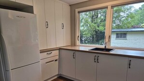 Una cocina con armarios blancos, un refrigerador empotrado, un ventanal con vistas a árboles y suelo de madera.
