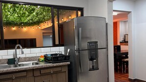 Une cuisine moderne dotée d’un réfrigérateur en acier inoxydable, d’un plan de travail en granit, de meubles en bois et d’une fenêtre donnant sur un paysage verdoyant.