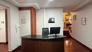 Un espace d’accueil avec un comptoir de réception en bois, un téléphone et un écran d’ordinateur. Les murs sont ornés de tableaux encadrés et un mur est mis en valeur par un revêtement en briques.