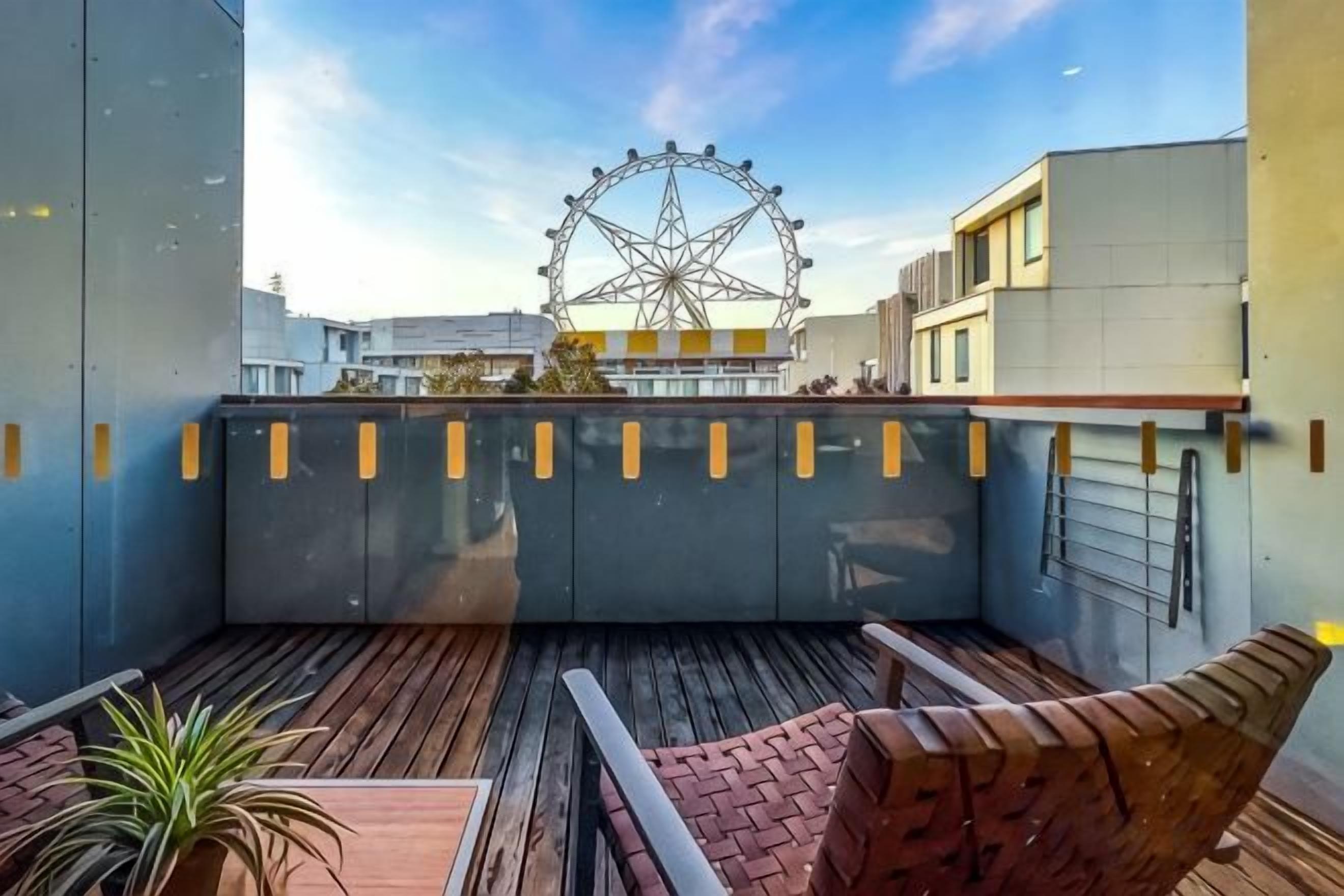 Une terrasse sur le toit offrant une vue sur une grande roue, avec un plancher en bois et un mur en briques.