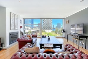 A modern living room with a large window, a sofa, a dining table, and a fireplace. - Lux Docklands District 3-level TH FreeParking (Docklands)
