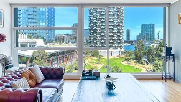 Un salon moderne doté d’une grande fenêtre, d’un canapé en cuir, d’une table basse et offrant une vue sur les bâtiments de la ville et la verdure.