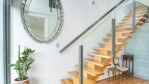 Un escalier avec des marches en bois et une rampe en verre, un grand miroir rond accroché au mur et une plante en pot.