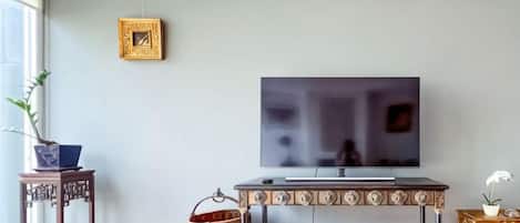 Una sala de estar con un televisor de pantalla plana montado en la pared, una mesa de centro de madera y una mesita auxiliar con una planta en maceta.
