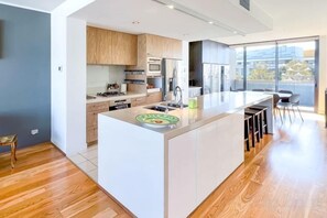 A modern kitchen with a central island, built-in appliances, and a large window providing a view of the city. - Lux Docklands District 3-level TH FreeParking (Docklands)