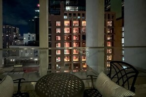 Een balkon met een glazen hekwerk, een ronde tafel en twee stoelen.