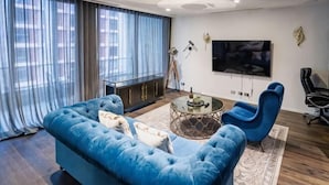 A modern living room with a blue sofa, a coffee table, and a TV mounted on the wall. - Luxury Melbourne CBD Apt in Iconic QT Hotel (Melbourne)