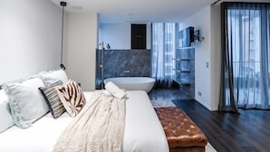 A modern bedroom with a large bed, a bedside table, a bench, a bathtub, and a walk-in closet. - Luxury Melbourne CBD Apt in Iconic QT Hotel (Melbourne)