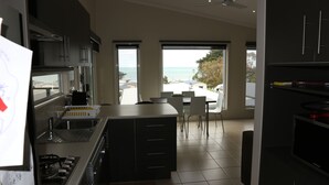 A modern kitchen with a view of the ocean, a dining area with chairs, and a large island. - Ultra-Modern Coastal Living (Apollo Bay)
