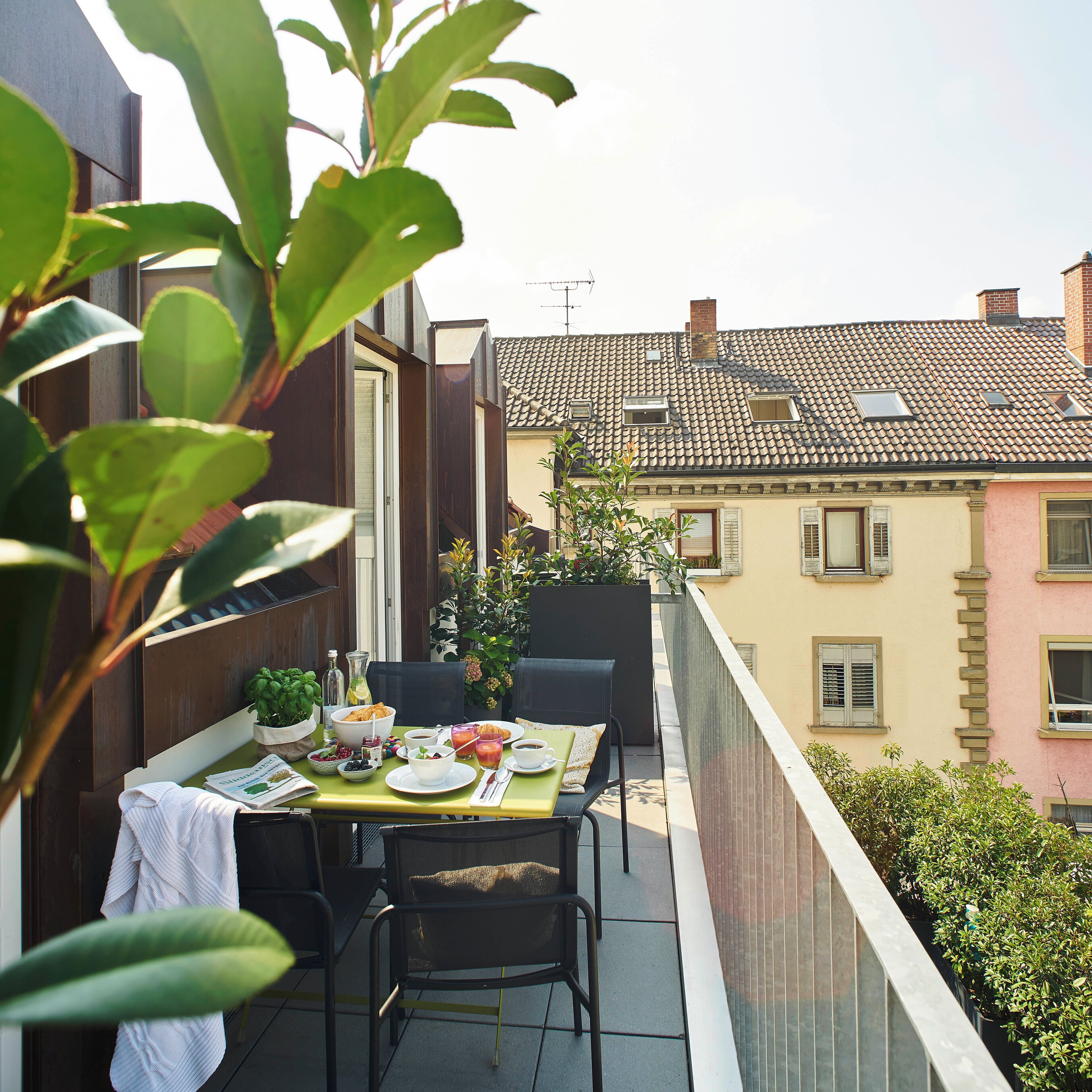 A balcony with a table set for breakfast, including plates, cups, and a bowl of fruit.