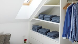 A bedroom with a skylight, a bed, a bedside table with books and a vase, a wardrobe with folded clothes, and a suitcase. - KÖNIGSschlaf's large vacation apartment for up to 3-5 people with sunny balcony (Konstanz)