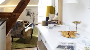 A cozy dining area with a wooden chair, a table set with croissants, a newspaper, and a vase with branches. - KÖNIGSschlaf's large vacation apartment for up to 3-5 people with sunny balcony (Konstanz)