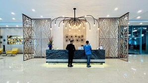 A reception desk with a marble top, surrounded by decorative panels and a modern chandelier. - BGC 1BR, Steps to Mitsukoshi & Uptown Malls, 300Mbps Fiber 19C2 (Taguig)