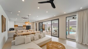 A modern interior with a sofa, dining table, and wicker ottoman. - Valentine Village (Koh Samui)