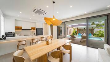 Una cocina moderna con armarios blancos, una mesa de comedor de madera y un ventanal con vistas a una zona de piscina.