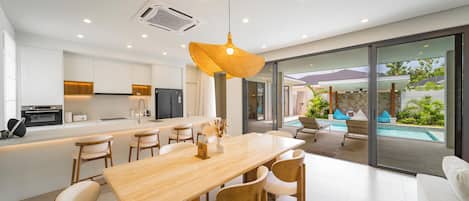 A modern kitchen with white cabinets, a wooden dining table, and a large window overlooking a pool area.