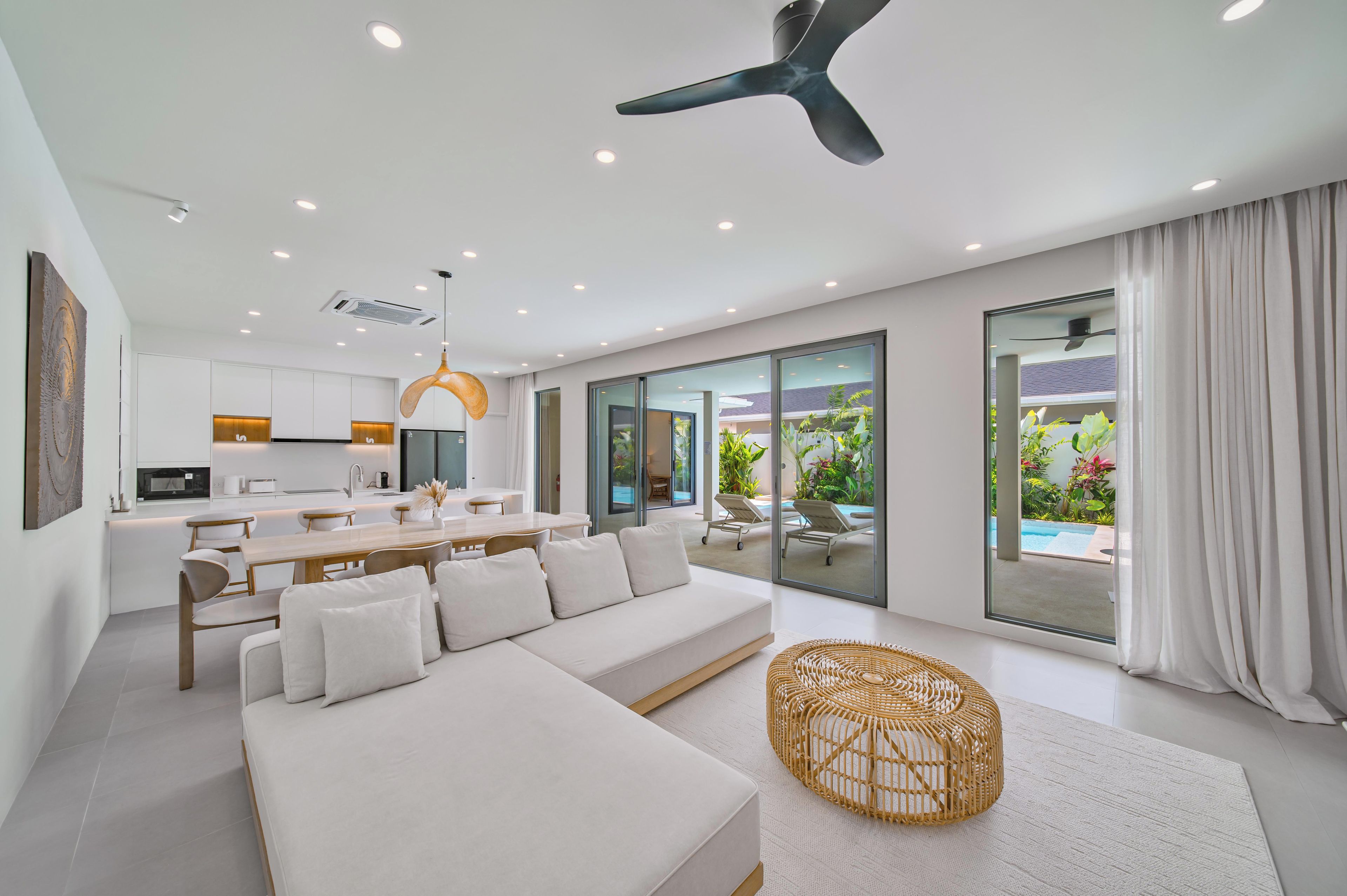 Ein modernes Wohnzimmer mit einer Couch, einem Essbereich und Blick auf einen Pool durch große Schiebetüren.