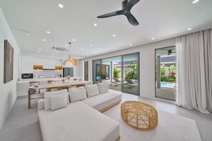Una sala de estar moderna con un sofá, comedor y vista a una piscina a través de amplios ventanales correderos.