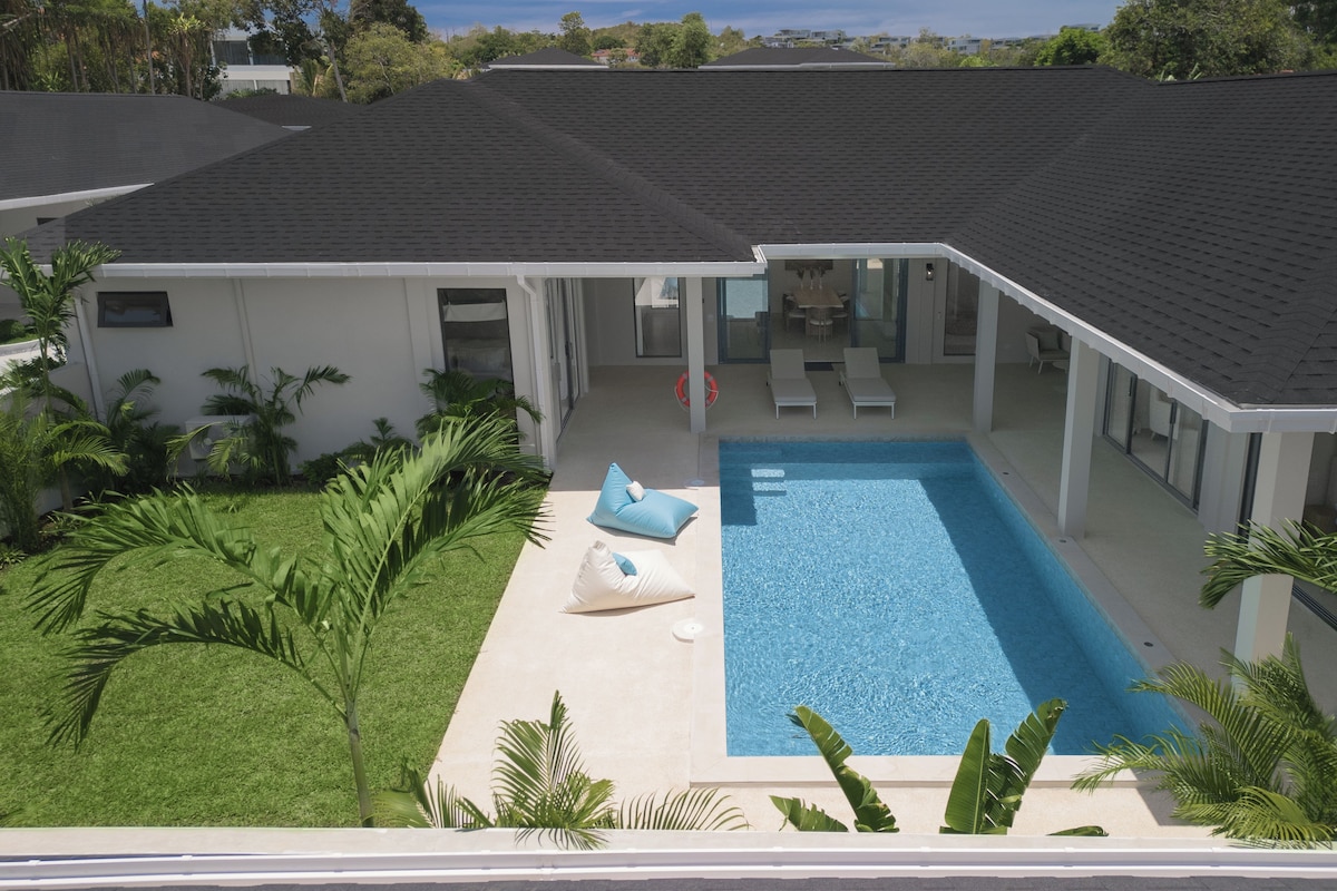 A residential building with a swimming pool, covered patio area, and surrounding greenery.