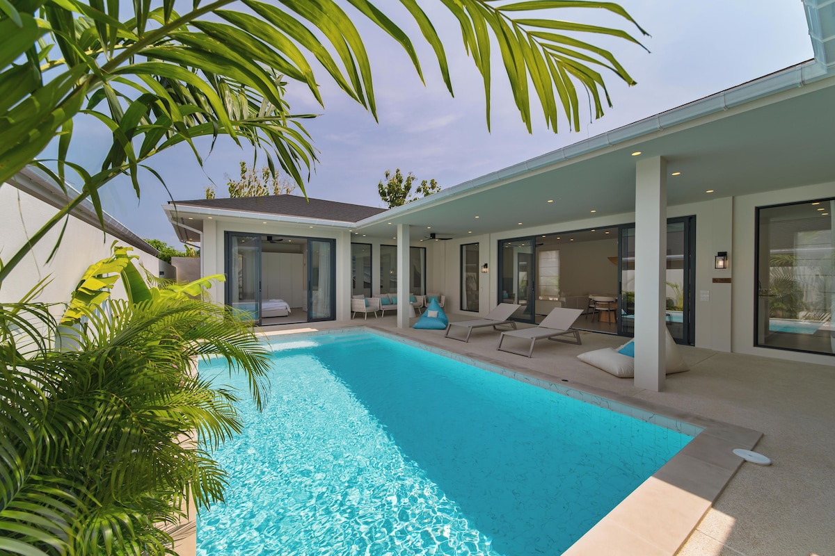 A modern poolside area with a clear blue pool, lounge chairs, and a covered patio.
