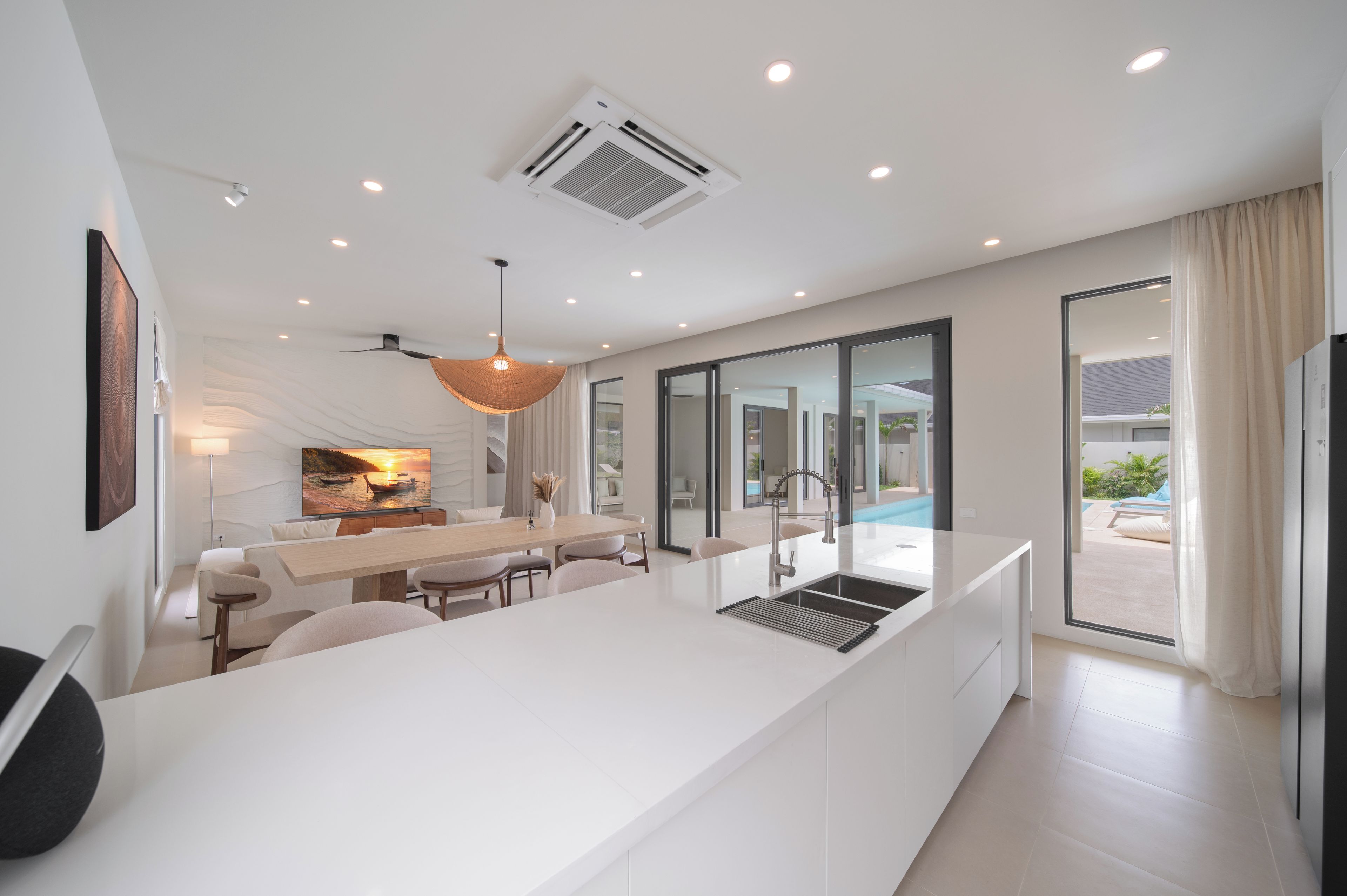 A modern kitchen with a central island, a dining area with a view of the outdoors, and a large window with curtains.