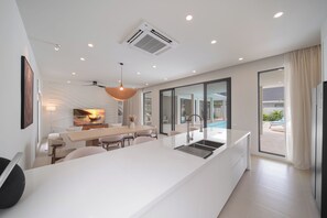 Una cocina moderna con una isla central, un comedor con vistas al exterior y un gran ventanal con cortinas.