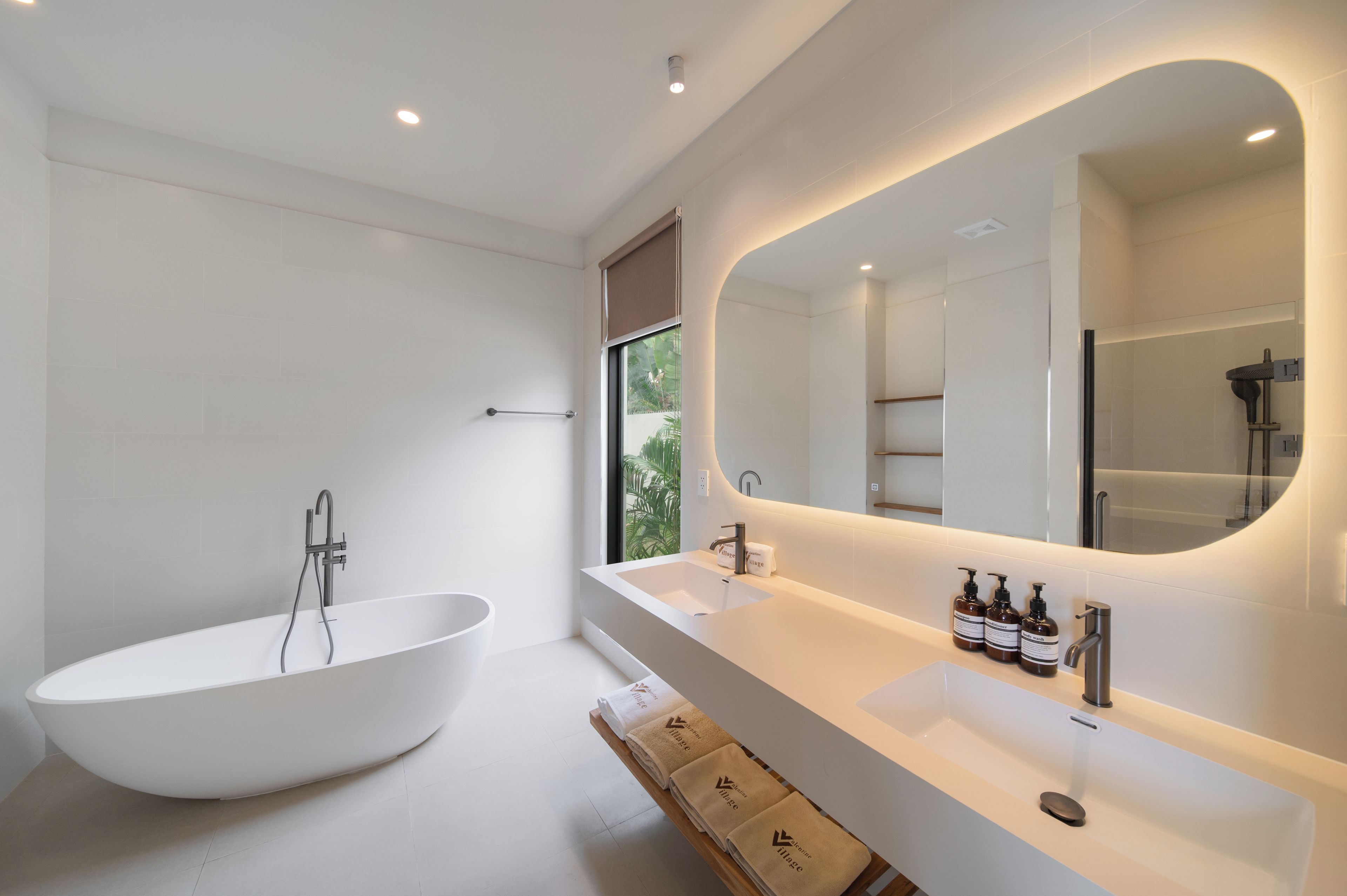 A modern bathroom with a freestanding bathtub, a large mirror, and a vanity with toiletries.